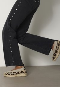 Luipaardprint espadrilles met een jute zool en zwarte accenten, gecombineerd met zwarte jeans met zilveren studs langs de zijnaad.