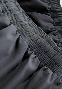 Schwarzer Stoff mit glatter Textur und einem vertikal verlaufenden gerafften Gummiband. Der Stoff fällt weich und zeigt einen dezenten Glanz.