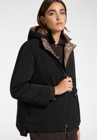 Giacca nera impermeabile con fodera a stampa leopardata, cappuccio, zip frontale e tasche. Presenta un tessuto leggero e una vestibilità rilassata.