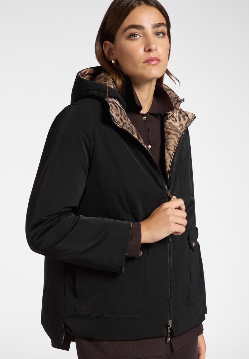Giacca nera impermeabile con fodera a stampa leopardata, cappuccio, zip frontale e tasche. Presenta un tessuto leggero e una vestibilità rilassata.