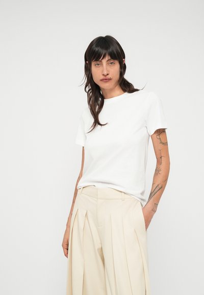 Biele bavlnené tričko s okrúhlym výstrihom, krátkymi rukávmi a voľným strihom, skombinované s béžovými plisovanými nohavicami.