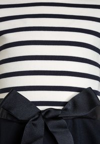 Camisa de rayas horizontales en blanco y negro combinada con un cinturón de tela negro atado en un lazo en la cintura.