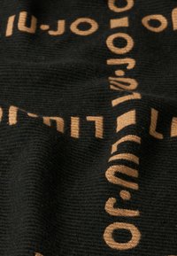 Tessuto nero con testo intrecciato beige in un motivo ripetuto, con una superficie testurizzata che crea una sottile profondità visiva.