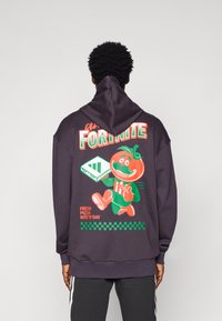 Sweatshirt roxo escuro com uma gráfica colorida de um personagem tomate a segurar um console de jogos, com o texto "FRESH PIZZA NITE'N'DAY."