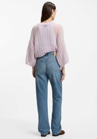 Maglione lavorato a maglia di colore lilla chiaro con maniche ampie e larghe, indossato sopra jeans blu a vita alta con una toppa sul retro e dettagli di cuciture sottili.