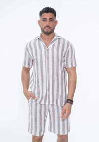 Chemise en lin à rayures à manches courtes et shorts assortis en brun clair et blanc. Fermeture bouton, coupe décontractée, texture visible dans le tissu.