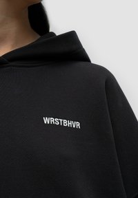 Czarna bluza z kapturem z kieszenią kangurzą i wytłoczonym białym logo "WRSTBVR" na piersi. Gładka faktura materiału.
