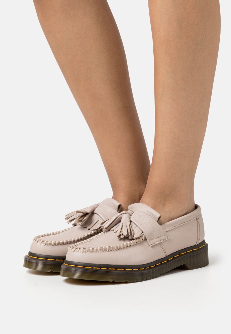 Des chaussures en cuir rose clair au design mocassin, avec des détails en franges et des coutures jaunes sur une semelle foncée. Elles présentent une coupe basse et une texture lisse.