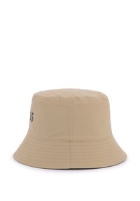 Chapeau seau beige avec une couronne plate et un bord incliné vers le bas. Fabriqué en tissu léger, il présente des accents cousus et un logo sur le côté.