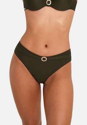 Femme portant un bas de bikini côtelé vert foncé avec un détail de boucle métallique rectangulaire sur la ceinture, sur fond uni.