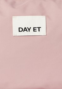 Rosa tekstureret stof med en hvid label, der står "DAY ET" i fede sorte bogstaver, syet i det øverste venstre hjørne.