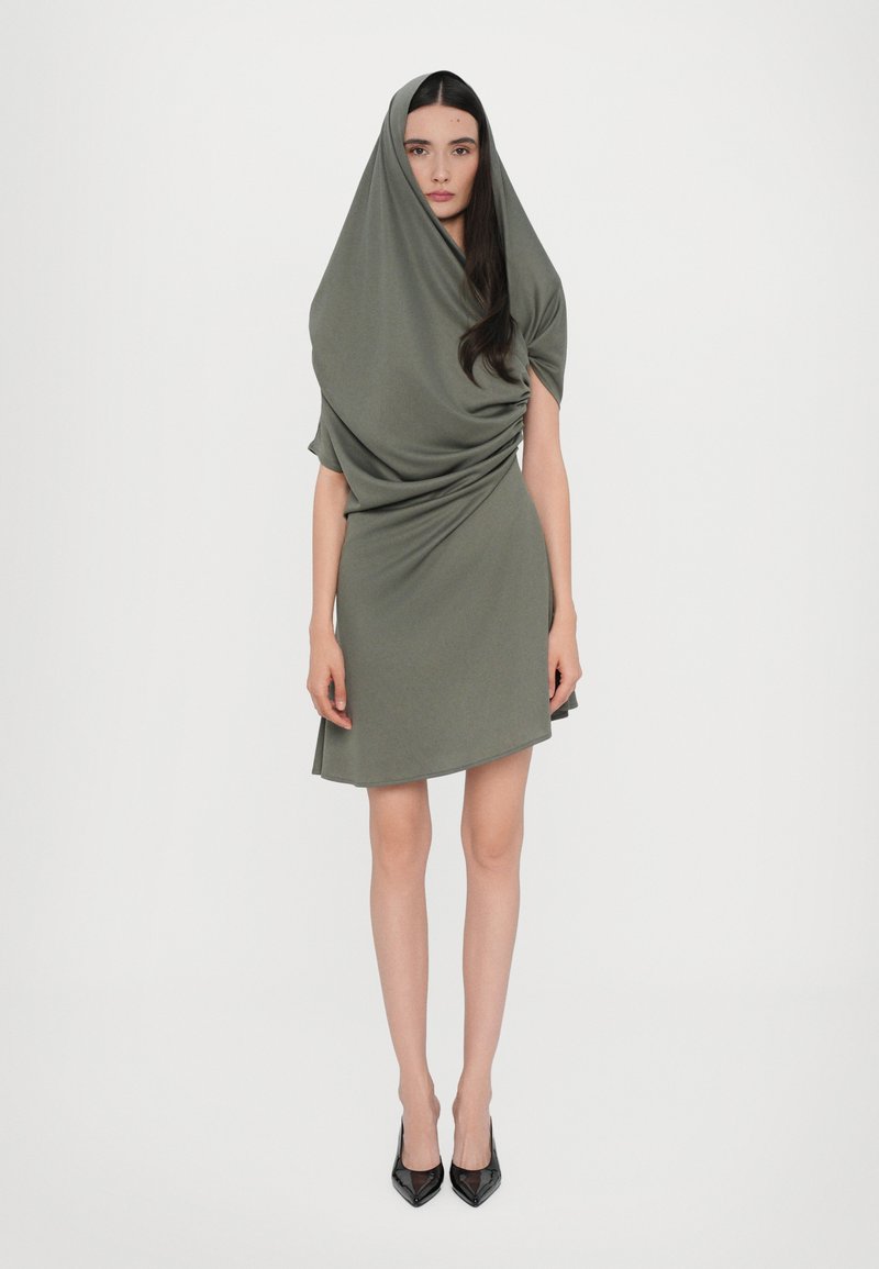 Olive green dress made of soft fabric, featuring draped design with a hood and short sleeves, paired with black pointed-toe heels.