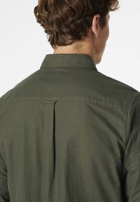Camisa verde oliva abotonada con un cuello clásico, pliegue trasero simple y una textura de tela suave. Diseño simple y funcional.