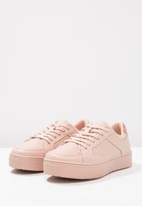 Ljusrosa syntetiska sneakers med snörningsdesign, rund tå, texturerad gummisula och mönstrad bakre detalj. Slät yta genom hela skon.