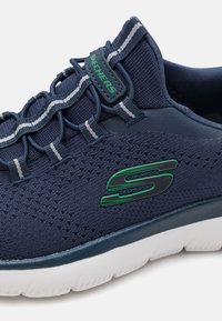Skechers shoes featuring a navy mesh upper with perforations, elastic lacing system, and a green logo accent. Cushioned white sole.