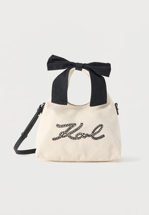 Sac à main en tissu beige avec inscription "Karl" en perles noires, anse en tissu avec nœud noir et bandoulière noire amovible.