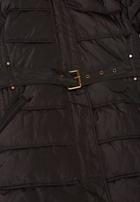 Veste matelassée noire avec coutures horizontales, ceinture en tissu assorti avec boucle dorée, et poches latérales bordées de noir.