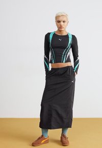 Svart långärmad tröja med turkosa detaljer och figursydd design, parat med en svart kjol, bruna skor och teal-strumpor. Sportmärke-logga synlig.