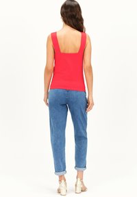 Rode mouwloze top met een brede vierkante halslijn, gecombineerd met lichtblauwe jeans met opgerolde manchetten en zilveren blokhakken sandaal.