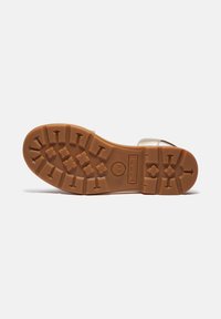 Brun gummisula med ett strukturerat greppmönster och Timberland-logotyp. Lätta metalliska accenter på ovankanten. Platt, öppen design.