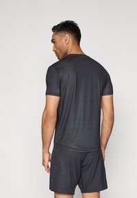 Σετ αθλητικών ρούχων σε σκούρο γκρι χρώμα, που αποτελείται από κοντομάνικη μπλούζα και σορτς με γεωμετρικό σχέδιο σε όλο το ύφασμα, φτιαγμένα από αναπνεύσιμο υλικό.