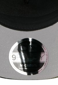 Graue 9FORTY-Cap mit schwarzen Akzenten, verstellbares A-Frame-Design, ausgestattet mit einem glänzenden silbernen Etikett mit Marken- und Modellangaben.