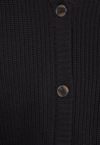 Tissu en tricot noir avec bande de boutonnage côtelée et deux grands boutons ronds foncés attachés verticalement au centre.