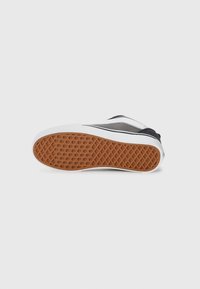 Basket noire et blanche avec une semelle en caoutchouc texturée présentant un motif en nid d'abeille, tige en synthétique, col rembourré et un branding minimal.