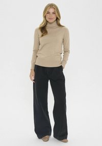 Jasno beżowy sweter z golfem i długimi rękawami, w zestawieniu z luźnymi czarnymi spodniami. Stylizacja zawiera płaskie buty z ćwiekami.