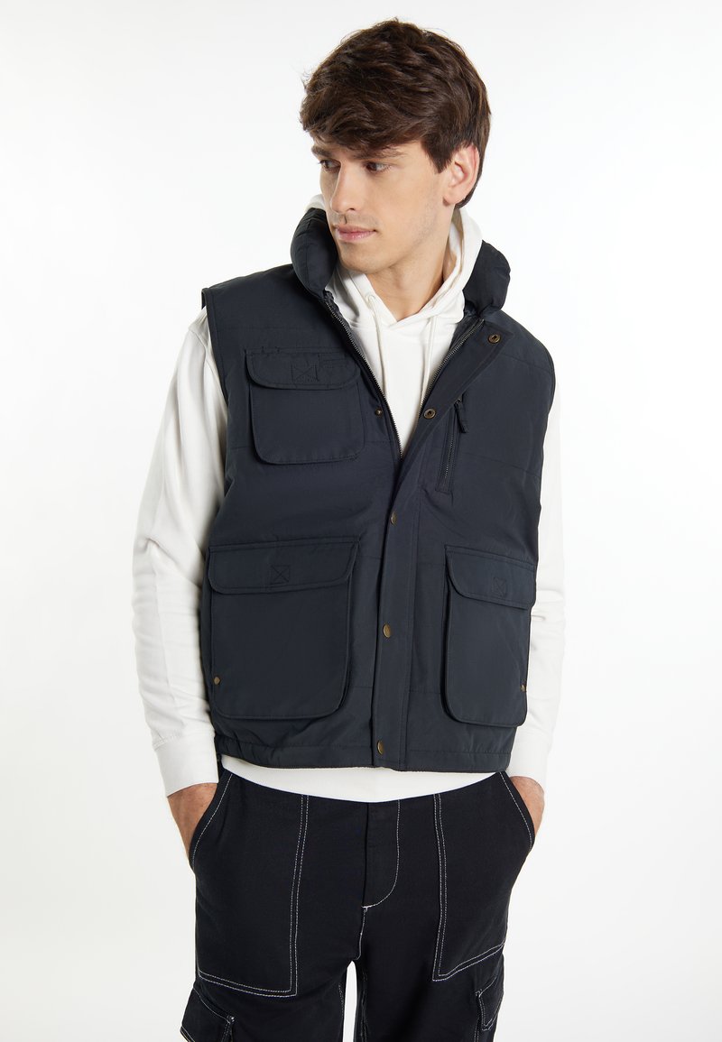 Gilet blu navy con cappuccio, multiple tasche frontali e chiusura con zip. Realizzato in tessuto leggero e morbido con una texture liscia.