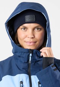 Kurtka wodoodporna w granatowym i jasnoniebieskim kolorze, z kapturem, zapinana na zamek, z regulowanymi mankietami oraz oddychającego materiału o gładkiej fakturze.