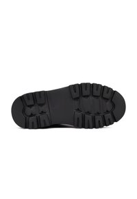 Suela de zapato de goma negra con un patrón de tracción robusto, con profundos surcos y elementos de acolchado para mayor agarre y comodidad.