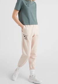 Puuvillainen keskipitkä teal-sininen t-paita, jossa on "Women of the Wave" -printti, ja vaaleanpunaiset collegehousut, joissa on sama printti sekä joustavat lahkeensuut ja vyötärönauha.