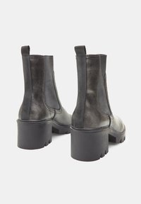 Botas de cuero negro hasta el tobillo con paneles laterales elásticos, tacones más gruesos, textura suave y tiradores rectangulares para facilitar el uso.