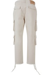 Pantalones cargo beige con dos grandes bolsillos laterales, parches traseros, puños elásticos y un cordón en el dobladillo. Fabricados con un material resistente.