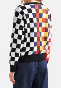 Färgglad tröja med ett schackrutigt mönster i svart, vitt och livfulla nyanser. Mjukt stickat material med svart ribbad fåll.