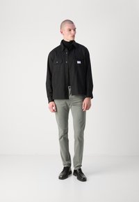 Cămașă neagră cu nasturi, dotată cu două buzunare pe piept, asortată cu pantaloni slim-fit de un verde deschis și pantofi negri cu șireturi. Design curat și minimalist.