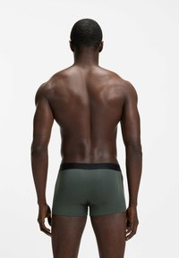 Green boxer shorts made of smooth fabric with a black waistband; model shown from behind against a plain white background.