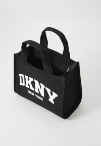 Black fabric tote bag with two handles, rectangular shape, white "DKNY NEW YORK" text on the front, zipper closure on top, textured surface.