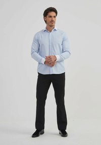 Chemise habillée à rayures bleu clair avec des poignets blancs, col classique et fermeture à boutons. Portée avec un pantalon noir et des chaussures noires.