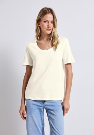 Krämfärgad bomulls t-shirt med bred rund halsringning, korta ärmar och avslappnad passform, i kombination med ljusblå denim. Slät struktur.