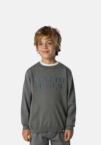 Grauer Baumwollpullover mit "NORTH SAILS" in blauer Schrift, Rundhalsausschnitt, langen Ärmeln und gerippten Bündchen. Getragen mit grauen Hosen.