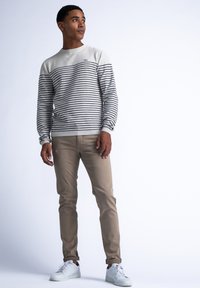 Suéter rayado en gris y blanco con cuello redondo, chinos beige y zapatillas blancas. Rayas horizontales prominentes y puños acanalados.