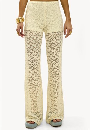 Pantalones de encaje crema de cintura alta con un estampado floral, llevados con pulseras de oro, anillos y zapatos de plataforma de punta abierta en azul claro.