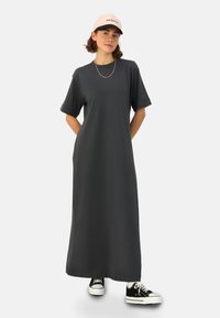 Robe maxi en tissu gris foncé, à manches courtes, coupe décontractée, avec poches latérales ; assortie à des baskets noires et une casquette rose.