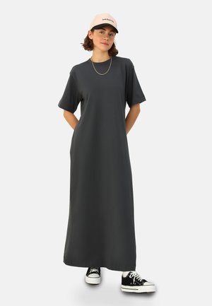 Abito maxi in tessuto grigio scuro, maniche corte, vestibilità ampia, dotato di tasche laterali; abbinato a sneakers nere e un cappellino rosa.