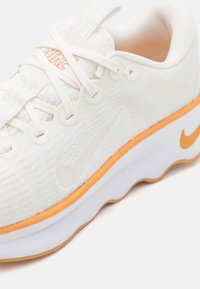 Chaussure de course Nike blanche avec des accents orange, dessus en tissu texturé, lacets blancs et semelle incurvée, vue de profil.
