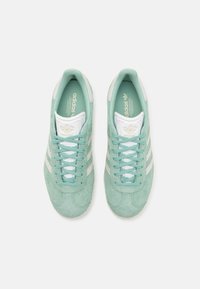 Zapatillas Adidas en suede verde menta claro con acentos en blanco, que presentan tres rayas blancas, diseño de cordones y superficie texturizada.