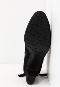 Zwarte suedine enkellaars met franjes en zijrits. Platte rubberen zool met een geperste merknaam en maat, die zorgt voor een gestructureerde grip.