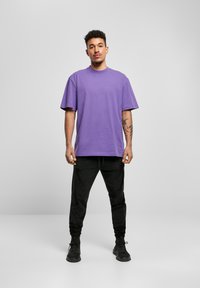 Tricou din bumbac mov, cu guler rotund și croială lejeră, asortat cu pantaloni jogger negri, mult mai îngustați și încălțăminte neagră. Design minimalist, fără modele.